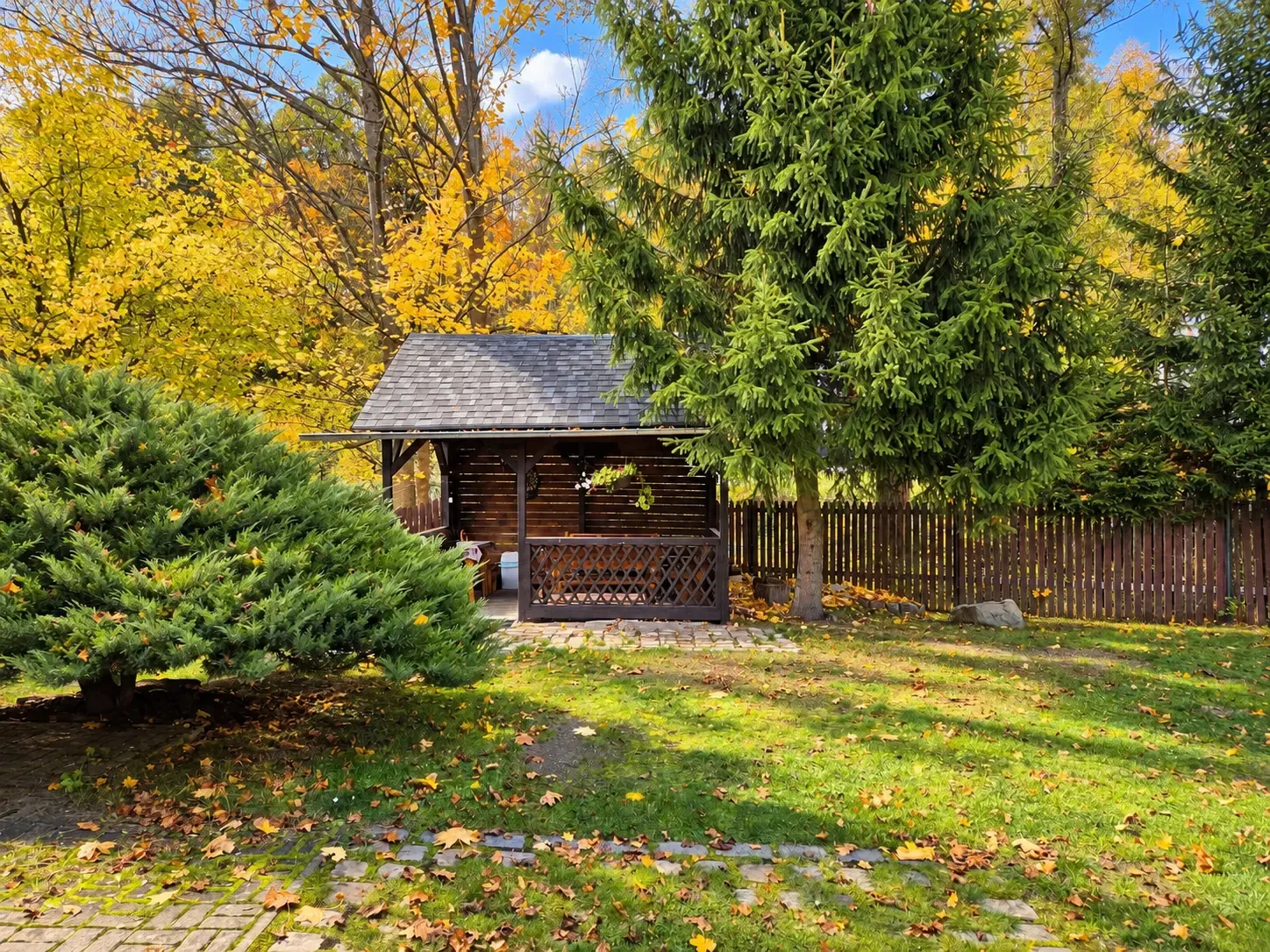 Der Herbstgarten des Hauses mit Holzaltan und sonnengelben Bäumen
